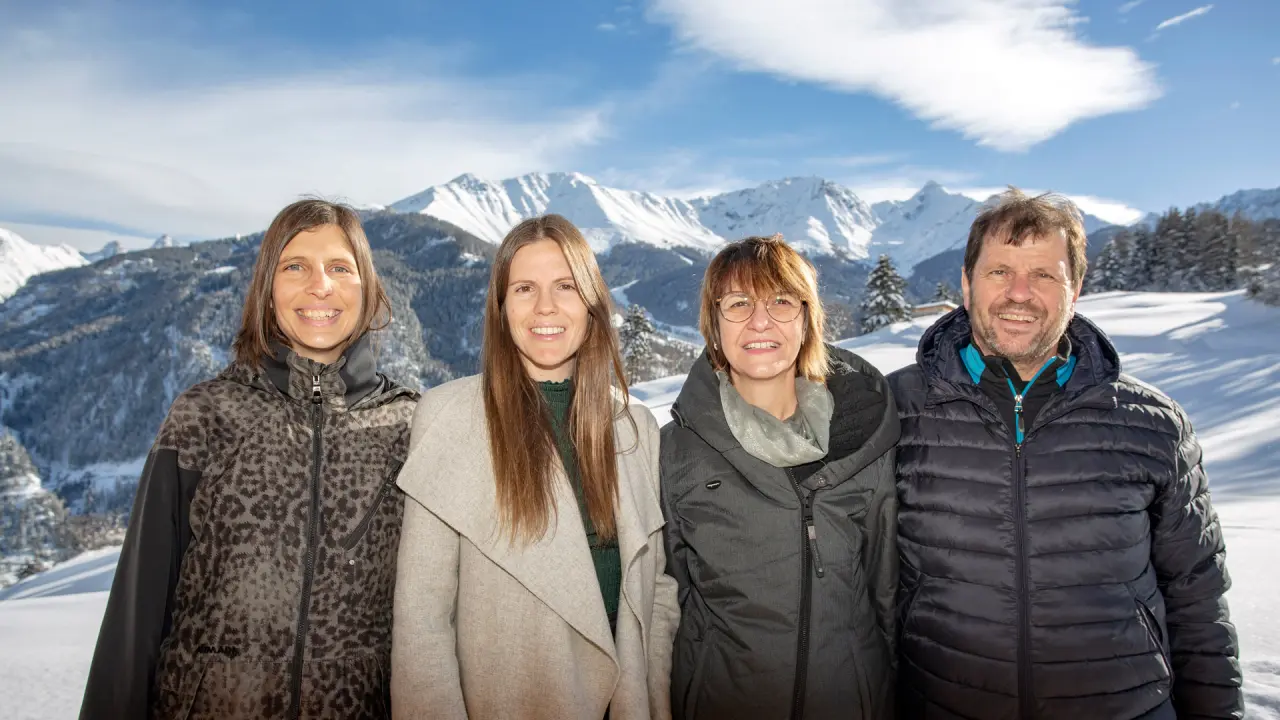Vier lächelnde Personen vor verschneiter Berglandschaft des Wellness- & Familienhotels Panorama.
