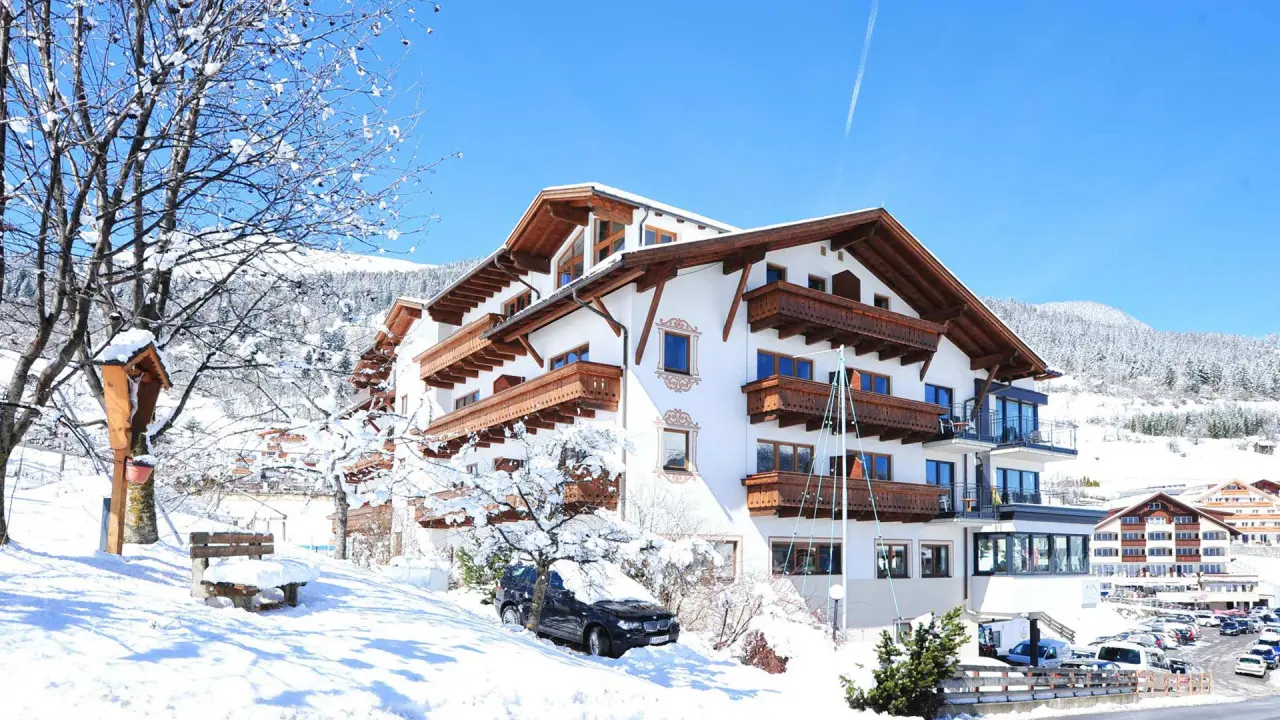 Winterliche Aussenansicht des Wellness- & Familienhotel Panorama im Alpenstil, umgeben von verschneiten Bergen und Bäumen.