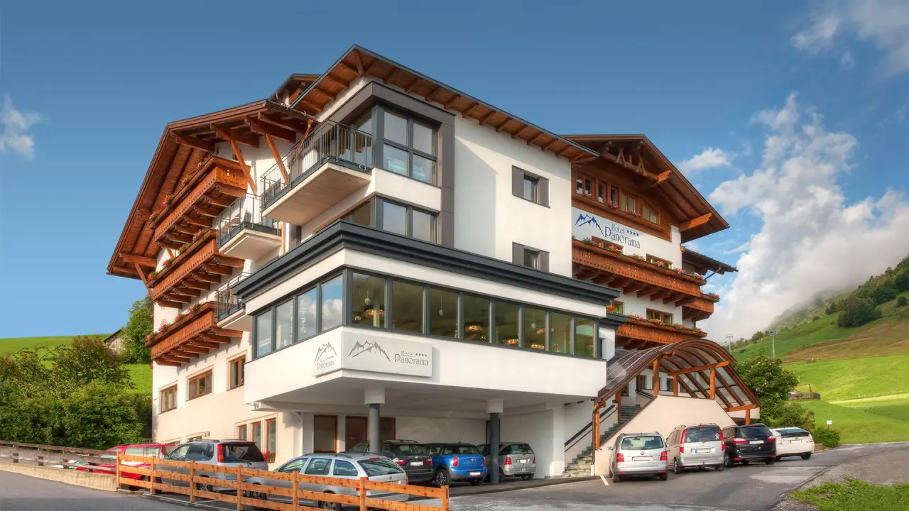 Aussenansicht des Wellness- & Familienhotels Panorama in den Bergen mit traditionellen Holzbalkonen und grüner Landschaft.
