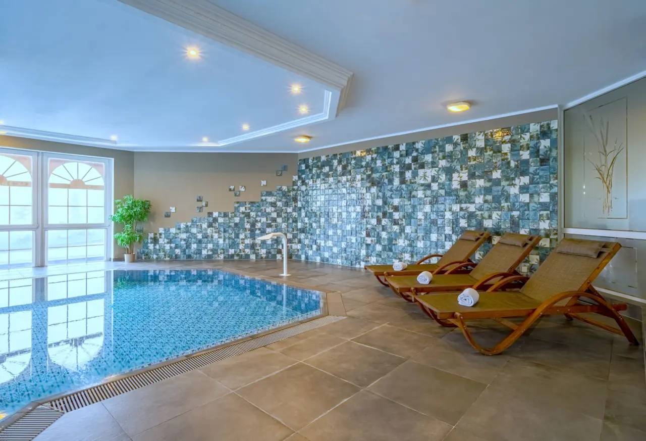 Einladender Innenpool mit bequemen Liegestühlen und großen Fenstern im Hotel Kammweg am Rennsteig.