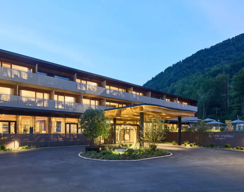 Modernes Hotel Sonne Mellau bei Abenddämmerung mit beleuchteter Fassade und Bergkulisse im Bregenzerwald.