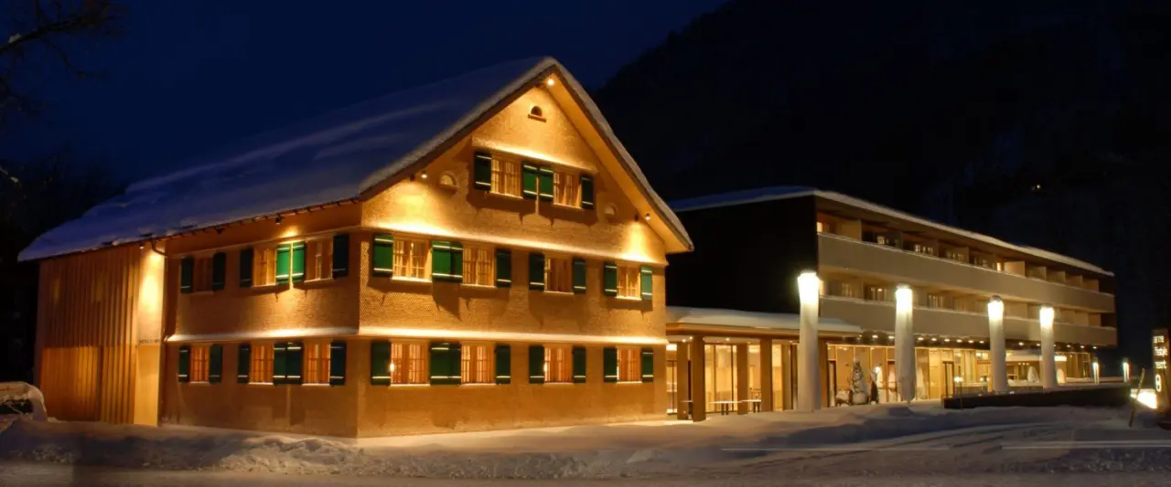Aussenansicht des Sonne Mellau - Feel good Hotel bei Nacht im Winter, mit verschneiten Dächern und warmer Beleuchtung.