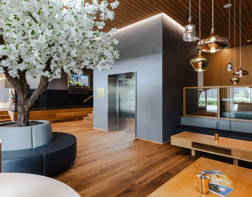 Moderne Hotellobby mit stilvoller Einrichtung, Holzfußboden und dekorativem Kirschblütenbaum im Sonne Mellau - Feel good Hotel.