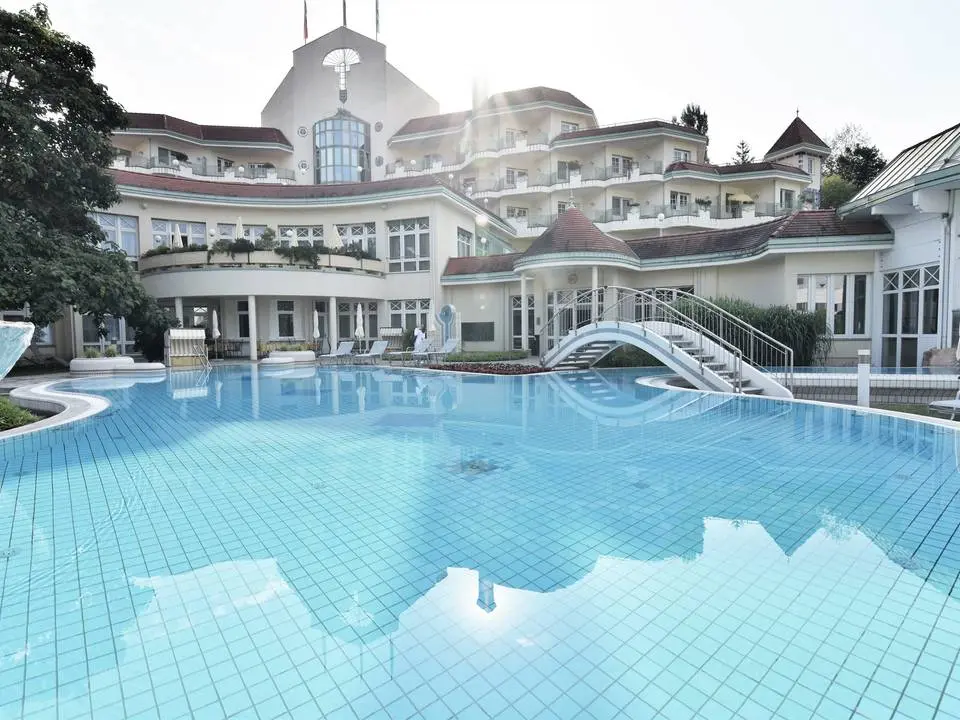 Weitläufiger Aussenpool mit Sonnenterrasse vor der eleganten Fassade des REDUCE Hotel Thermal ****S.