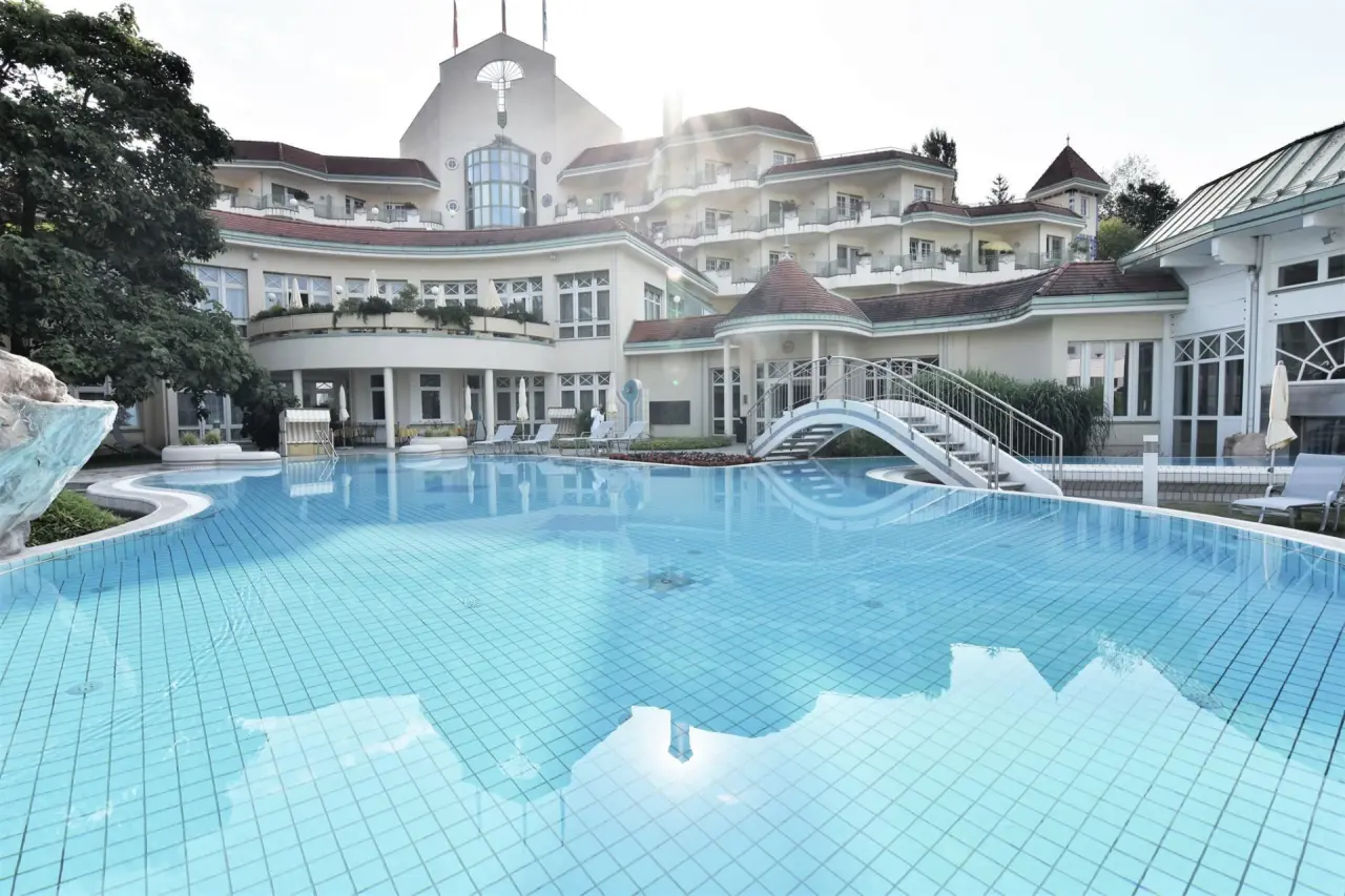Aussenansicht des REDUCE Hotel Thermal ****S mit weitläufigem Aussenpool und Sonnenterrasse an einem sonnigen Tag.