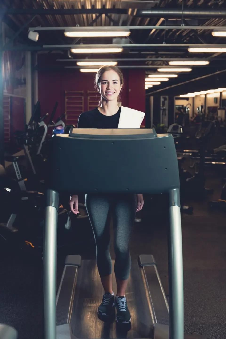 Junge Frau lächelt auf einem Laufband im modernen Fitnessbereich von Holzschuh’s Schwarzwaldhotel.