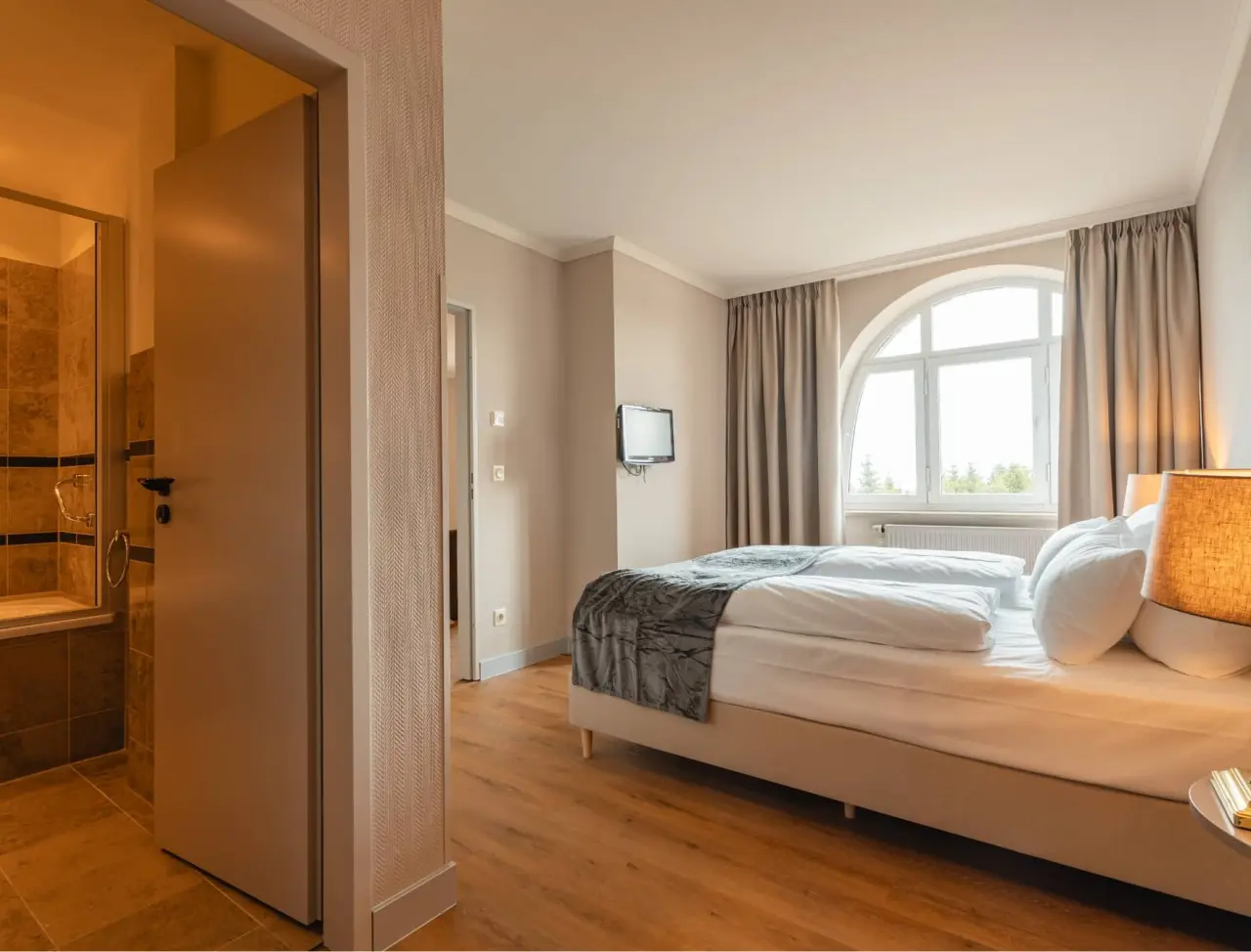 Gemütliches Doppelzimmer im Relaxhotel Sachsenbaude mit großem Bogenfenster und Blick ins Badezimmer.