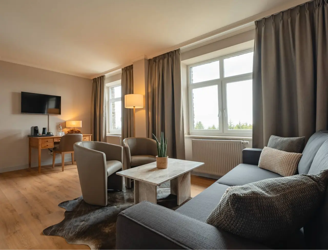 Gemütlicher Wohnbereich einer Suite im Relaxhotel Sachsenbaude mit Sofa, Sesseln und Schreibtisch.