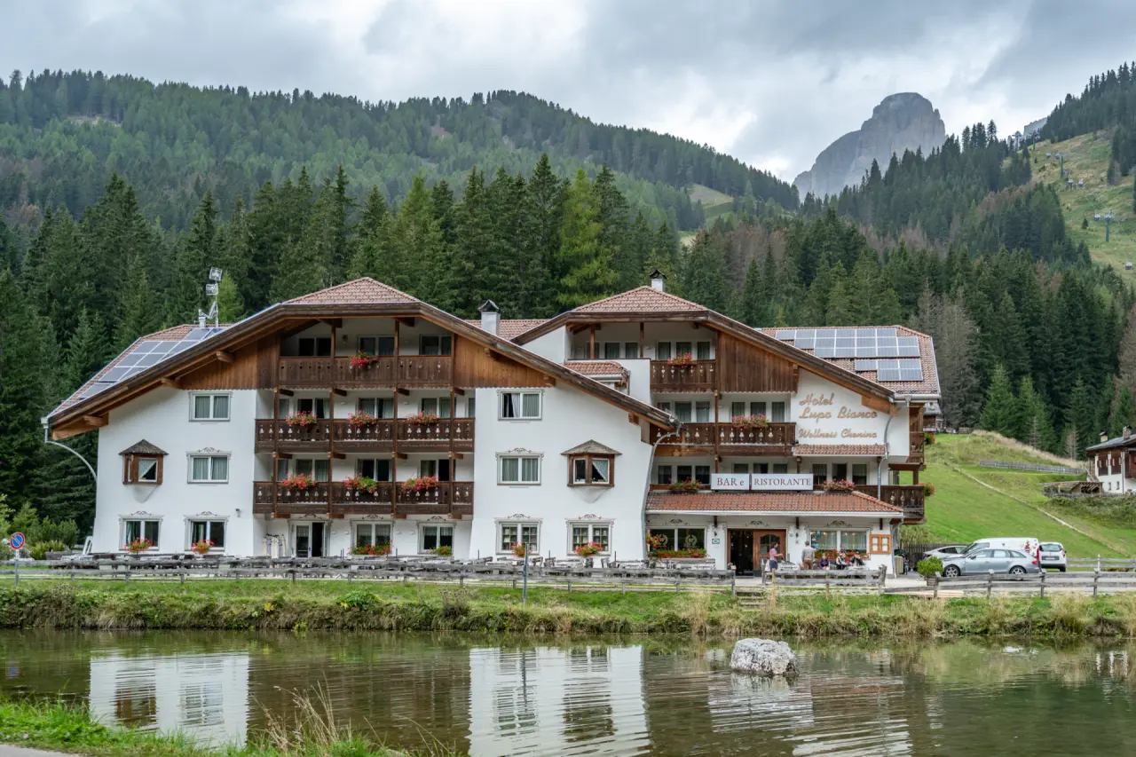 Hotel Lupo Bianco in Canazei – Außenansicht am See mit Bergpanorama | Wellnesshotel Dolomiten