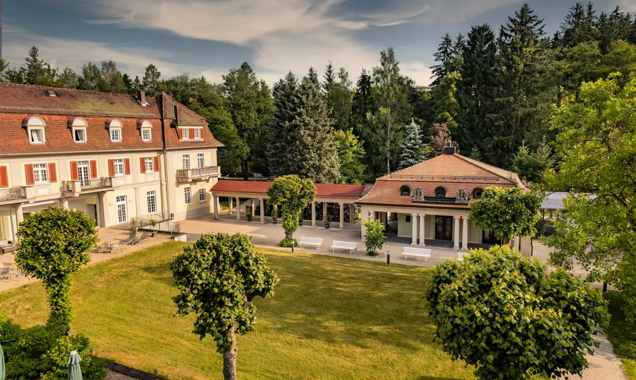 Historisches Hauptgebäude und Parkanlage des Hotel Sante Royale Bad Brambach umgeben von grünen Bäumen.