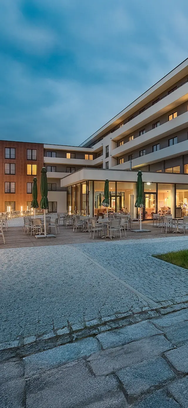 Moderne Aussenansicht des Hotel Sante Royale Bad Brambach bei Abenddämmerung mit beleuchteter Restaurantterrasse.
