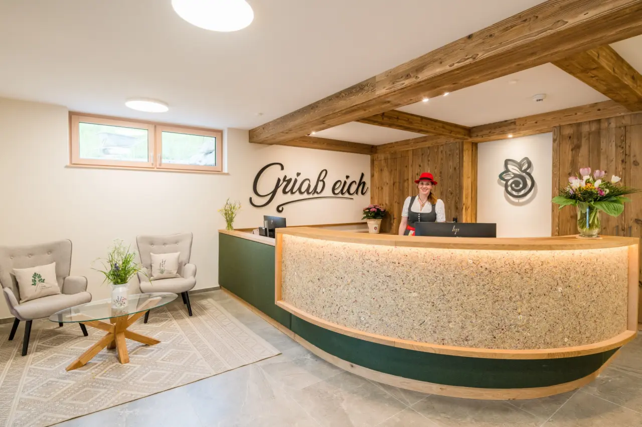 Herzlicher Empfangsbereich im Naturhotel Alpenrose mit Holzdesign, Sitzgelegenheiten und lächelnder Mitarbeiterin.