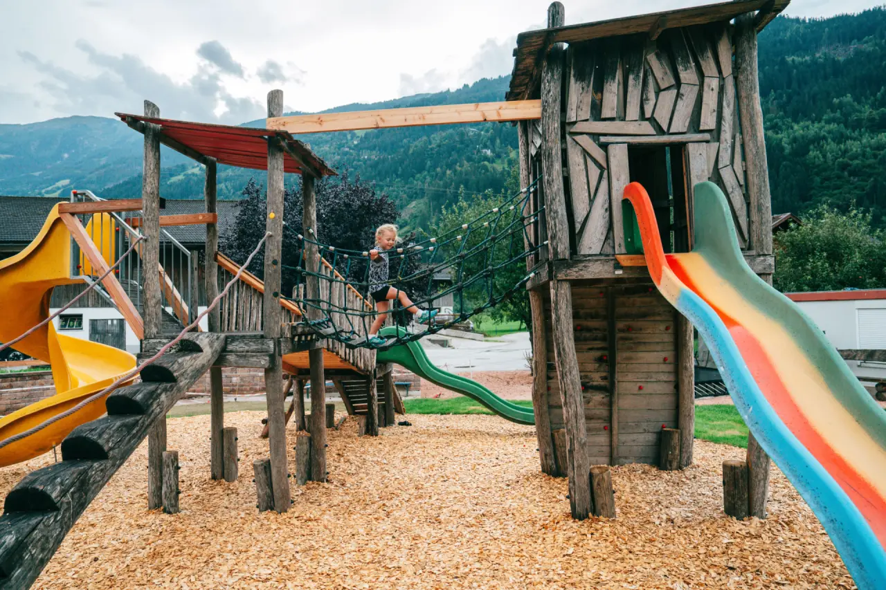 Kind spielt auf dem Holzspielplatz mit Rutsche und Kletternetz im Ferienhotel Sonnenhof****
