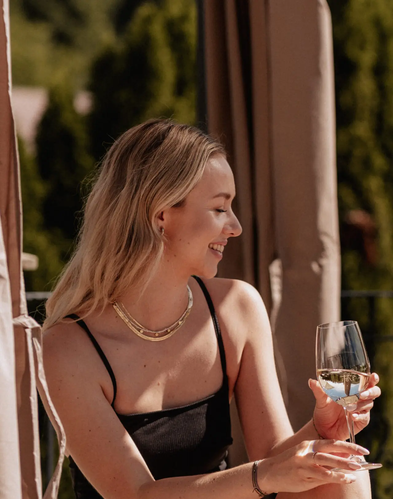 Lachende Frau genießt ein Glas Weißwein auf der sonnigen Terrasse des Schlössl Hotel Kindl. Entspannung im Wellnessurlaub.
