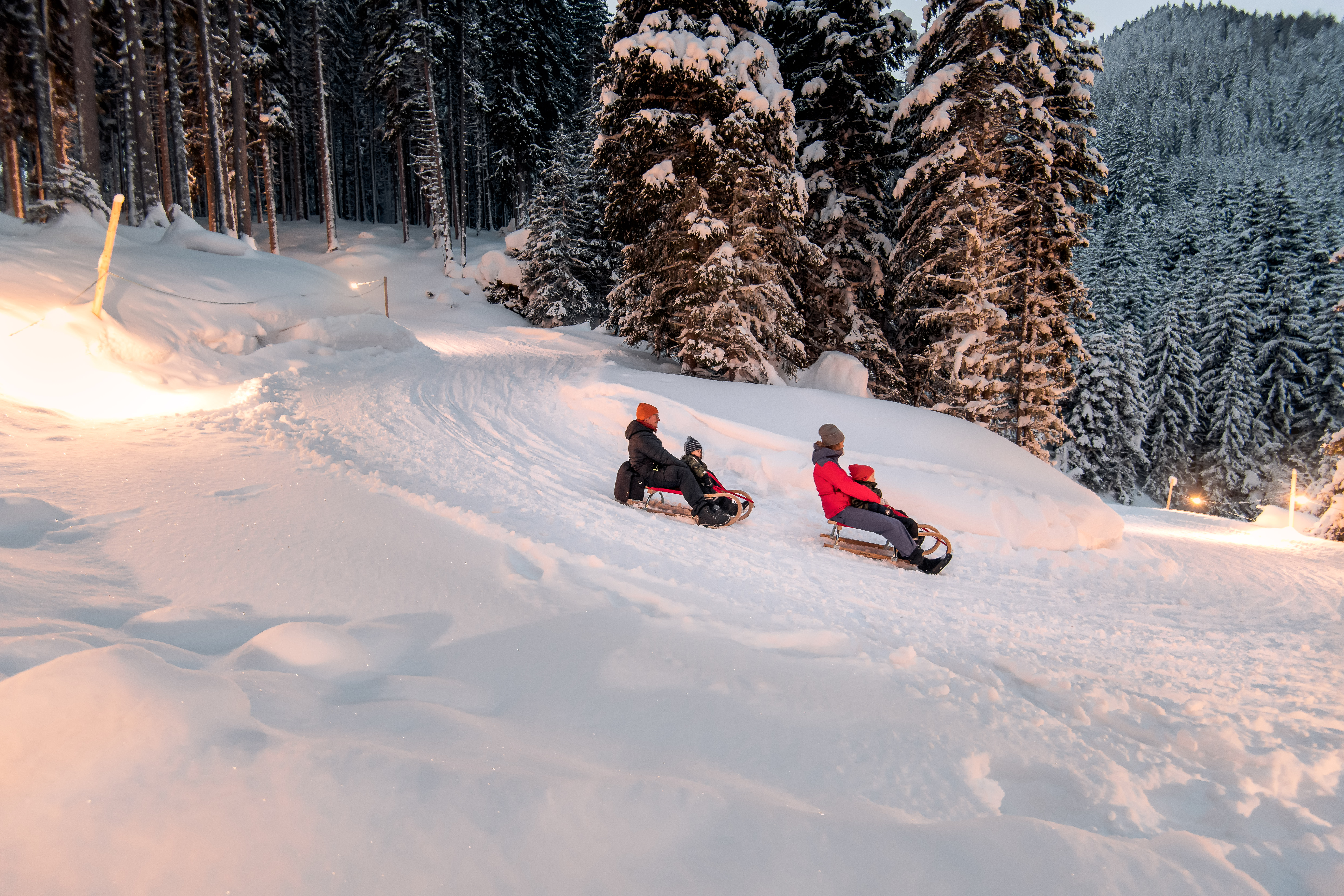 Das Alpenhaus Gasteinertal in Bad Hofgastein – Familie beim Rodeln im Schnee am Abend | Wellnesshotel Gasteinertal