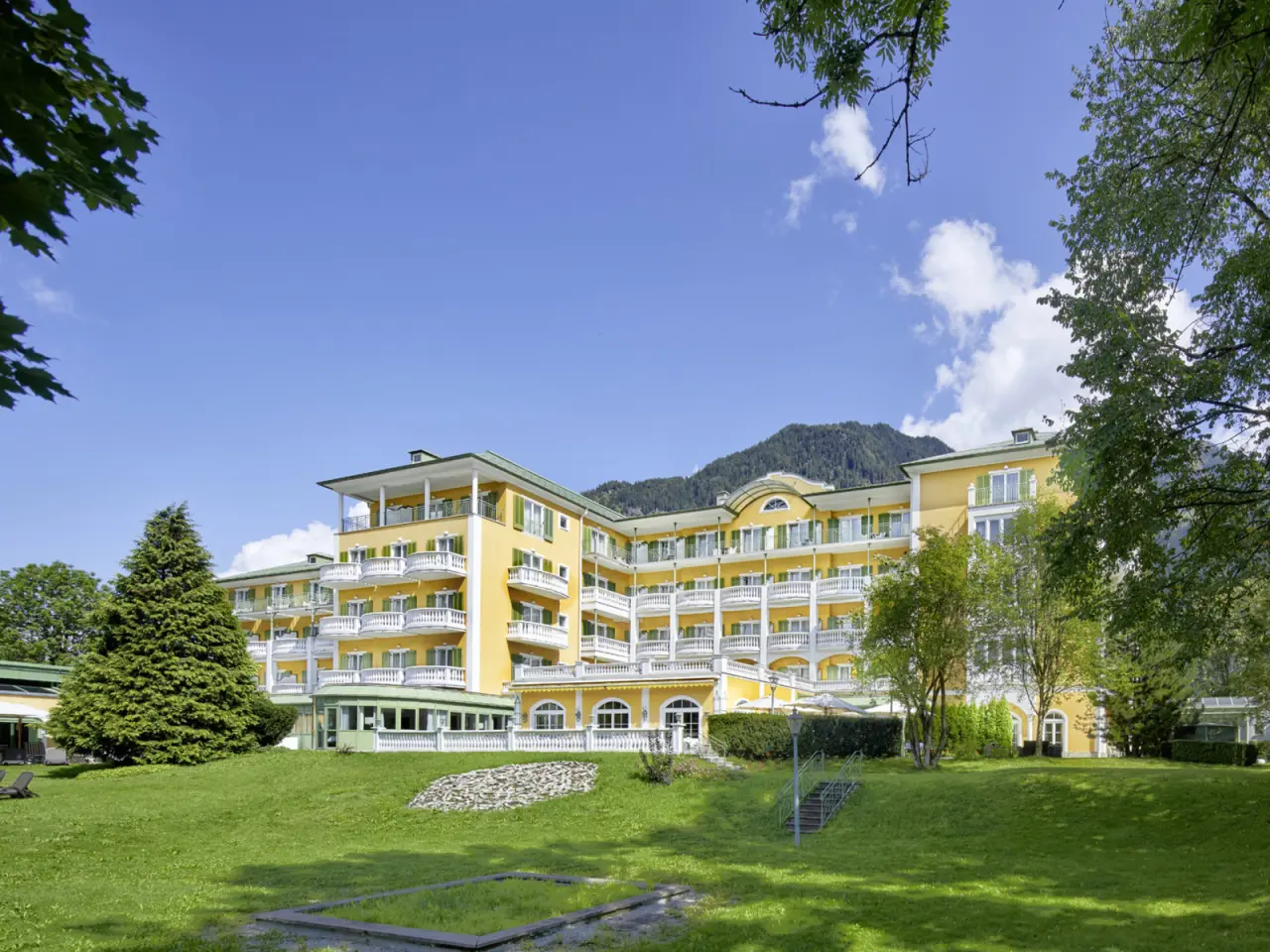 Aussenansicht des Alpenhaus Gasteinertal mit gelber Fassade, Balkonen und Bergpanorama im Sommer.