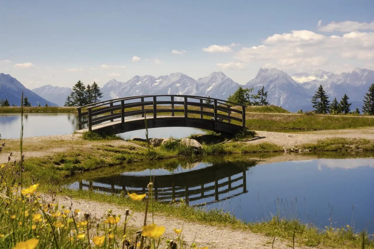 Hotel Seppl in Mutters – Holzbrücke über einen Teich mit majestätischem Bergpanorama | Wellnesshotel Tirol
