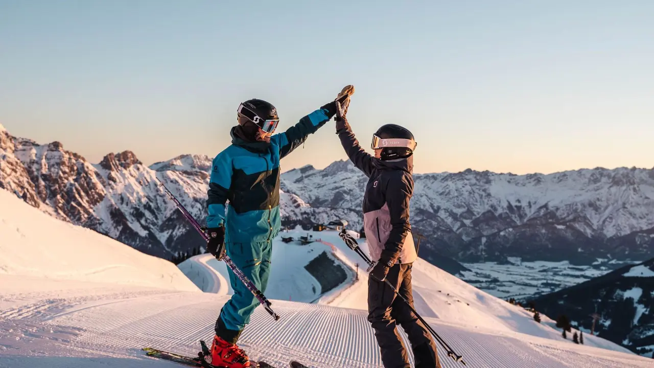 Zwei Skifahrer geben sich High-Five auf einer frisch präparierten Piste mit Bergpanorama bei Sonnenuntergang im Hotel Leonhard.