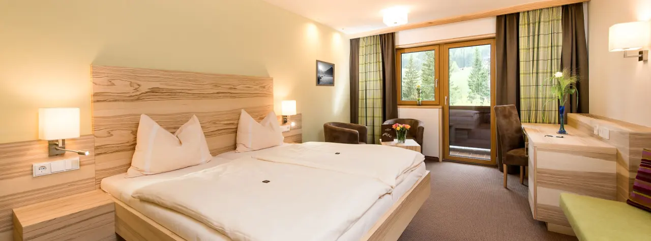 Gemütliches Doppelzimmer im Hotel Leonhard mit Holzelementen, Balkon und Blick ins Grüne.