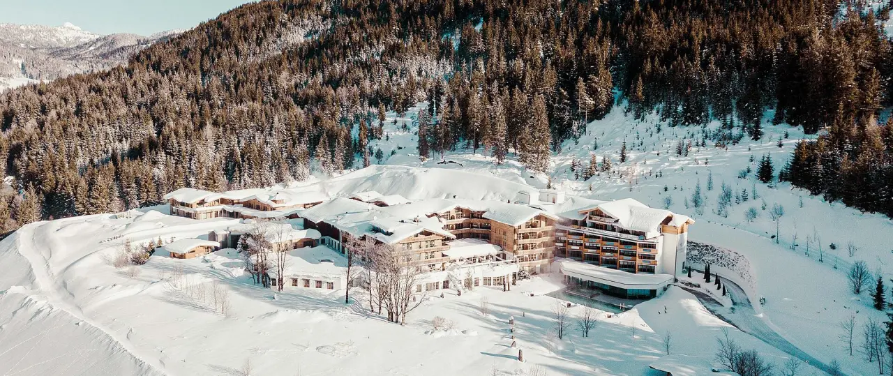 Luftaufnahme des Hotel Reiterhof im Winter, umgeben von verschneiten Bergen und Wäldern. Ein idyllisches Alpenresort.