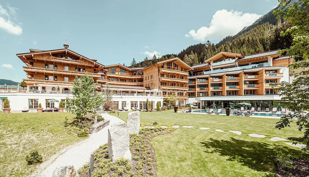 Grosszügiges Hotel Reiterhof mit traditioneller Holzarchitektur, Aussenpool und weitläufigem Garten vor alpiner Bergkulisse.