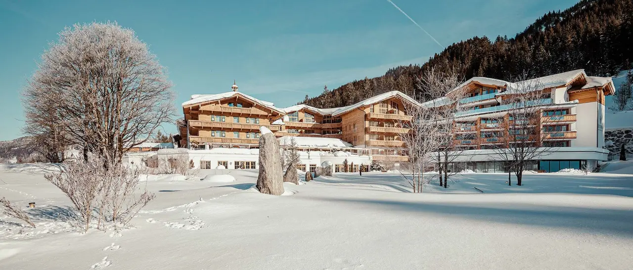 Winterliche Aussenansicht des Hotel Reiterhof in den verschneiten Alpen. Modernes Holzdesign, umgeben von gefrorenen Bäumen und Bergen.