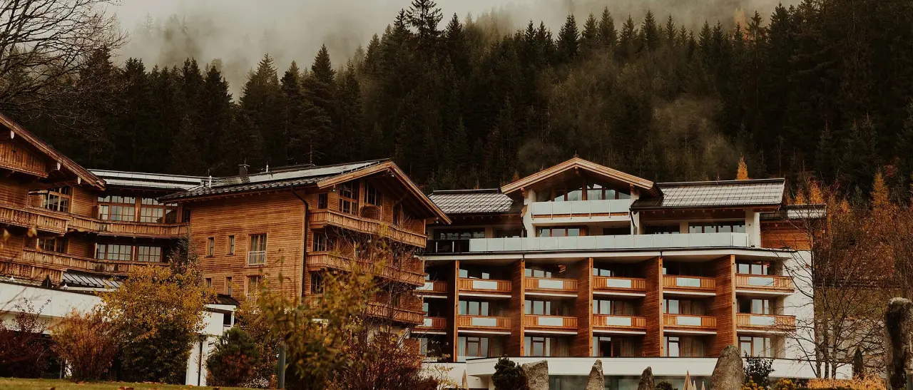 Hotel Reiterhof: Traditionelle Holzarchitektur im Herbstwald, umgeben von nebelverhangenen Bergen.