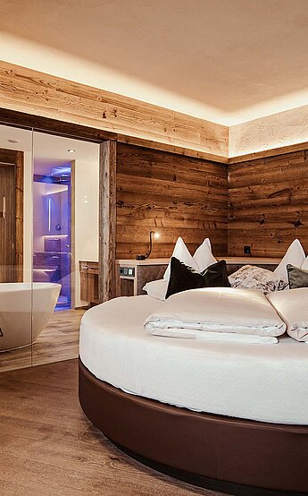 Luxuriöses Hotelzimmer im Hotel Reiterhof mit rundem Bett, Holzwänden und modernem Bad mit freistehender Wanne.