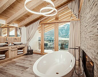 Luxuriöses Badezimmer mit freistehender Badewanne, Holzdecke und Bergblick im Hotel Reiterhof.