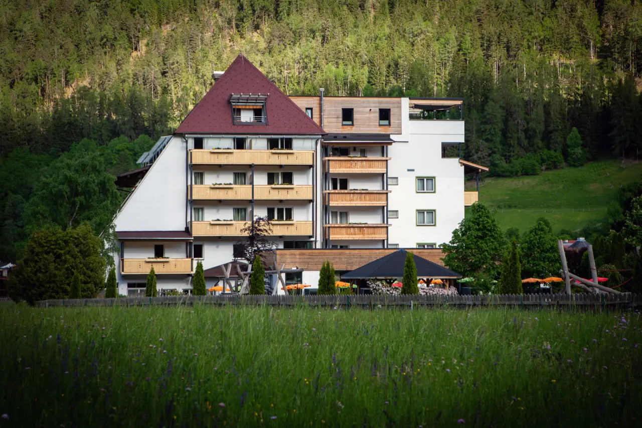 Aussenansicht des Hotel Truyenhof mit traditioneller Architektur vor bewaldetem Berghang und grüner Wiese.