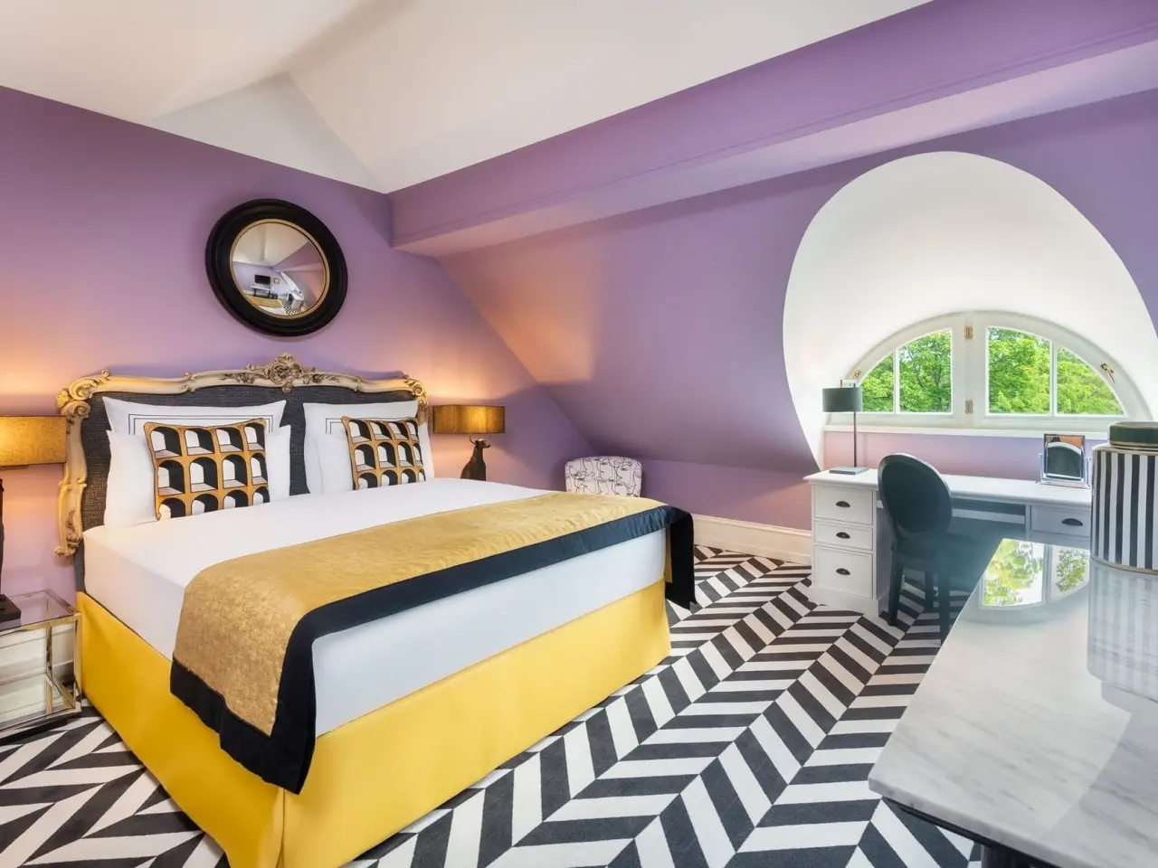 Stilvolles Hotelzimmer im Patrick Hellmann Schlosshotel mit lila Wänden, Chevron-Teppich und elegantem Bett.