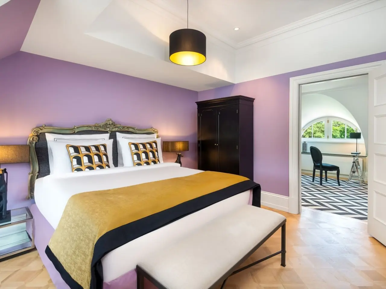 Luxuriöses Hotelzimmer mit lila Wänden, goldenem Bettüberwurf und stilvollem Dekor im Patrick Hellmann Schlosshotel.