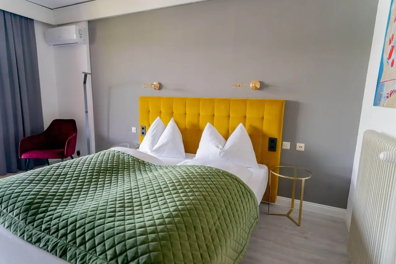 Modernes Doppelzimmer im Hotel Parks Velden mit gelbem Kopfteil und grüner Tagesdecke.