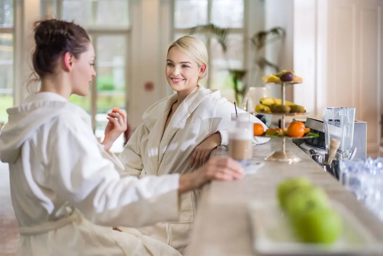 Zwei Frauen in Bademänteln genießen Getränke und frisches Obst an der Spa-Bar im Grand Hotel Heiligendamm.