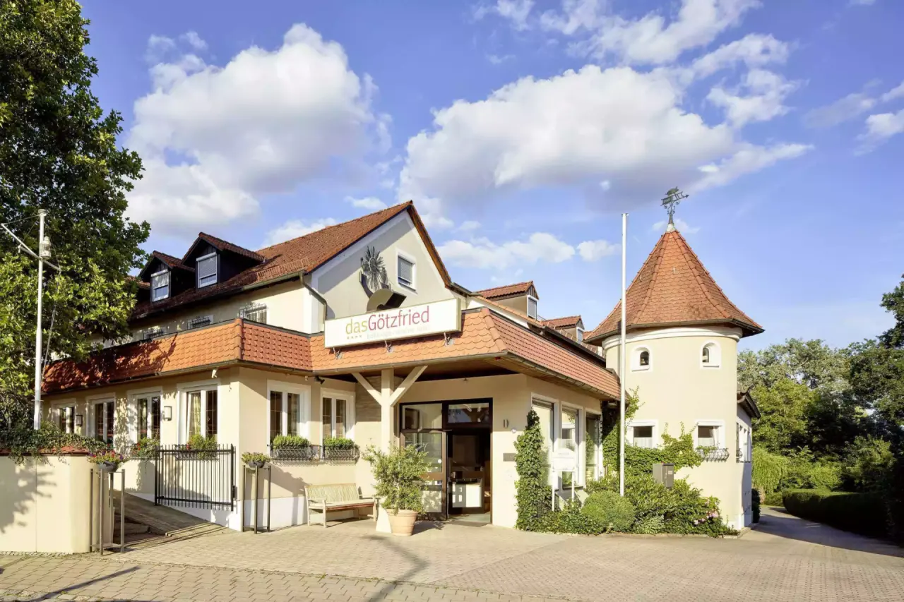 Aussenansicht des Götzfried**** Kultur- und Spahotels mit markantem Turm und einladendem Eingangsbereich unter blauem Himmel.