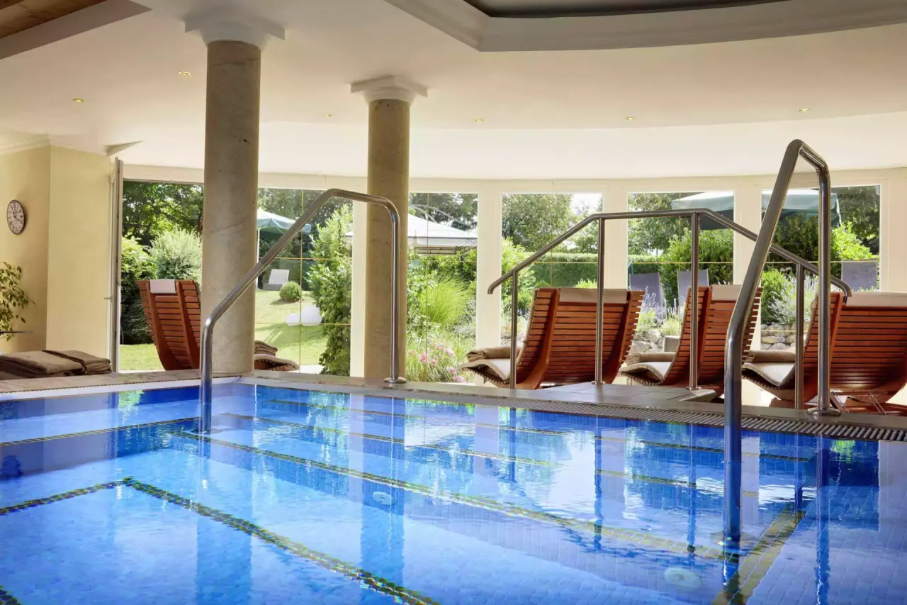 Einladender Innenpool mit Blick in den grünen Garten und bequemen Liegen im Das Götzfried**** Kultur- und Spahotel.