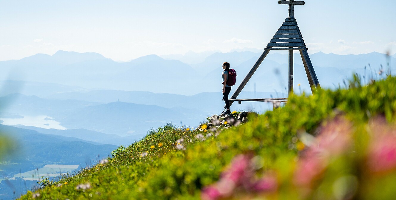 Feuerberg Mountain Resort in Bodensdorf/Gerlitzen Alpe – Wanderin am Gipfelkreuz mit Panoramablick | Wellnesshotel Kärnten