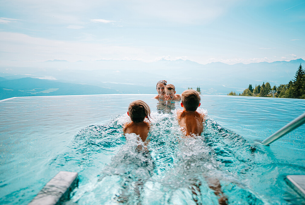 Feuerberg Mountain Resort in Bodensdorf/Gerlitzen Alpe – Familie im Infinity-Pool mit Bergblick | Wellnesshotel Kärnten