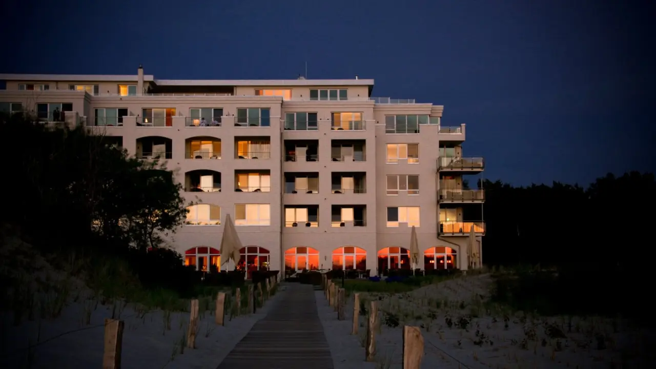 Abendliche Aussenansicht des Strandhotel Dünenmeer mit beleuchteten Fenstern und Zugangsweg durch die Dünen.