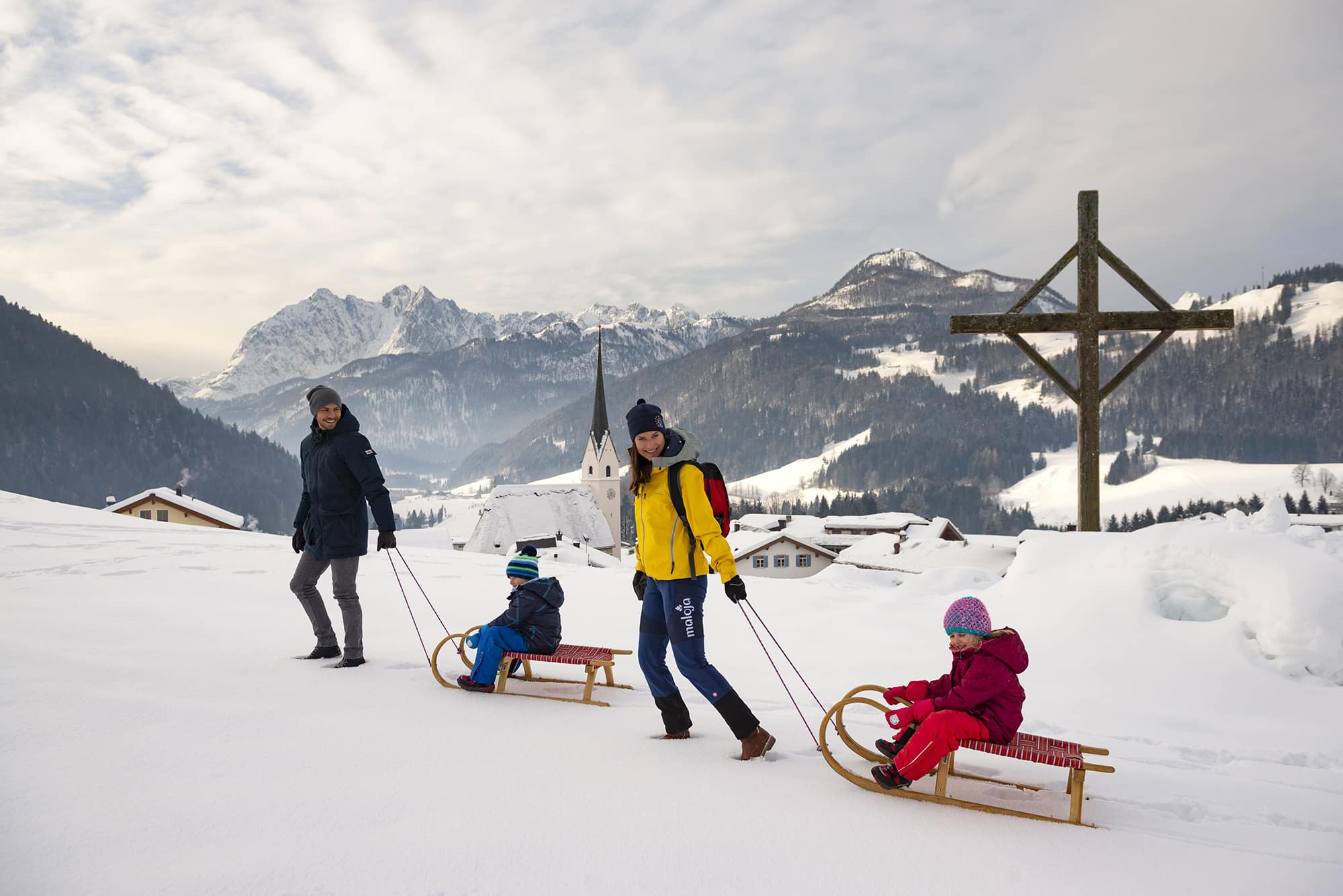 Hotel Seehof in Kössen – Familie beim Rodeln mit malerischem Dorf- und Bergpanorama | Wellnesshotel Tirol