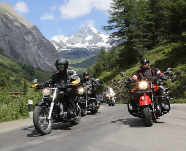 Motorradfahrer auf einer Bergstrasse mit schneebedeckten Gipfeln im Hintergrund, nahe dem Hotel Goldried.
