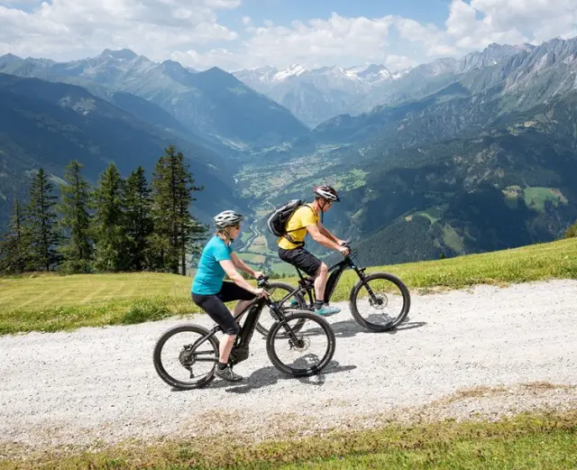Zwei E-Biker fahren auf einem Bergweg mit Panoramablick auf die Alpen im Umfeld des Hotel Goldried.