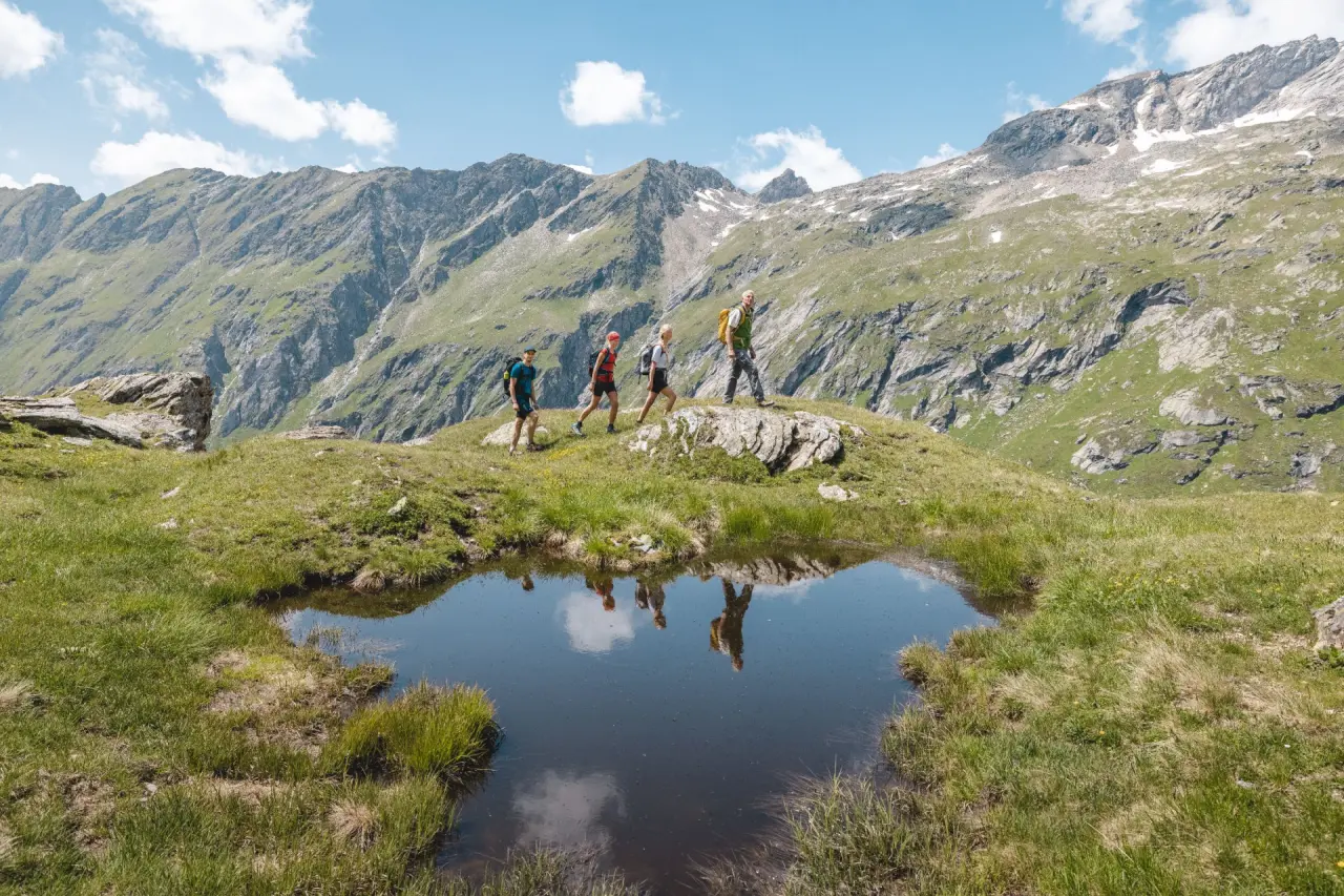 Wandergruppe in den Alpen mit Bergpanorama und kleinem Bergsee nahe Hotel Goldried