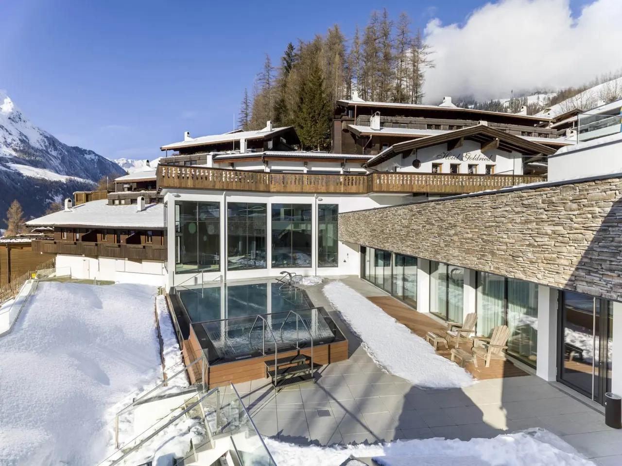Beheizter Aussenpool mit verschneiter Terrasse und Alpenpanorama am Hotel Goldried im Winter.