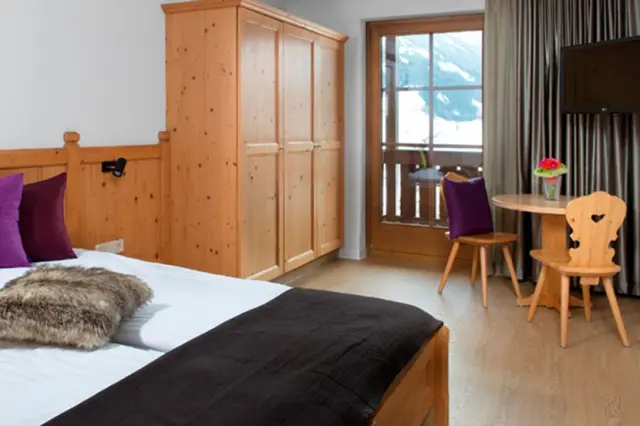 Gemütliches Hotelzimmer im alpinen Stil mit Holzeinrichtung, Doppelbett und Balkon mit Bergblick im Hotel Goldried.