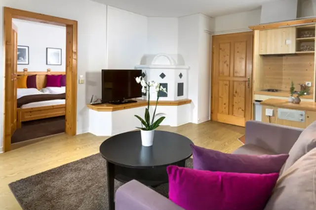 Gemütliches Wohnzimmer mit Kaminofen, Küchenzeile und Blick ins Schlafzimmer im Hotel Goldried.
