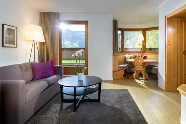 Helles Wohnzimmer mit Sofa, Essbereich und Panoramablick auf die Berge im Hotel Goldried.