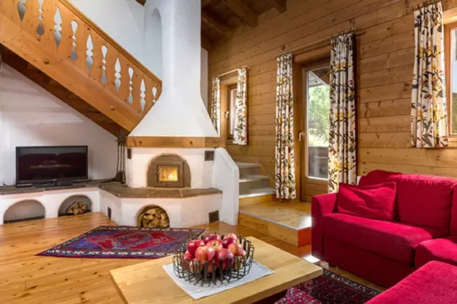 Gemütliches Wohnzimmer mit Kamin, rotem Sofa und Holzvertäfelung in einer Suite des Hotel Goldried.
