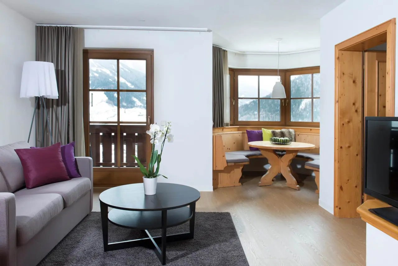 Gemütliches Hotelzimmer im Hotel Goldried mit Wohnbereich, Esstisch und Panoramablick auf die verschneiten Berge.