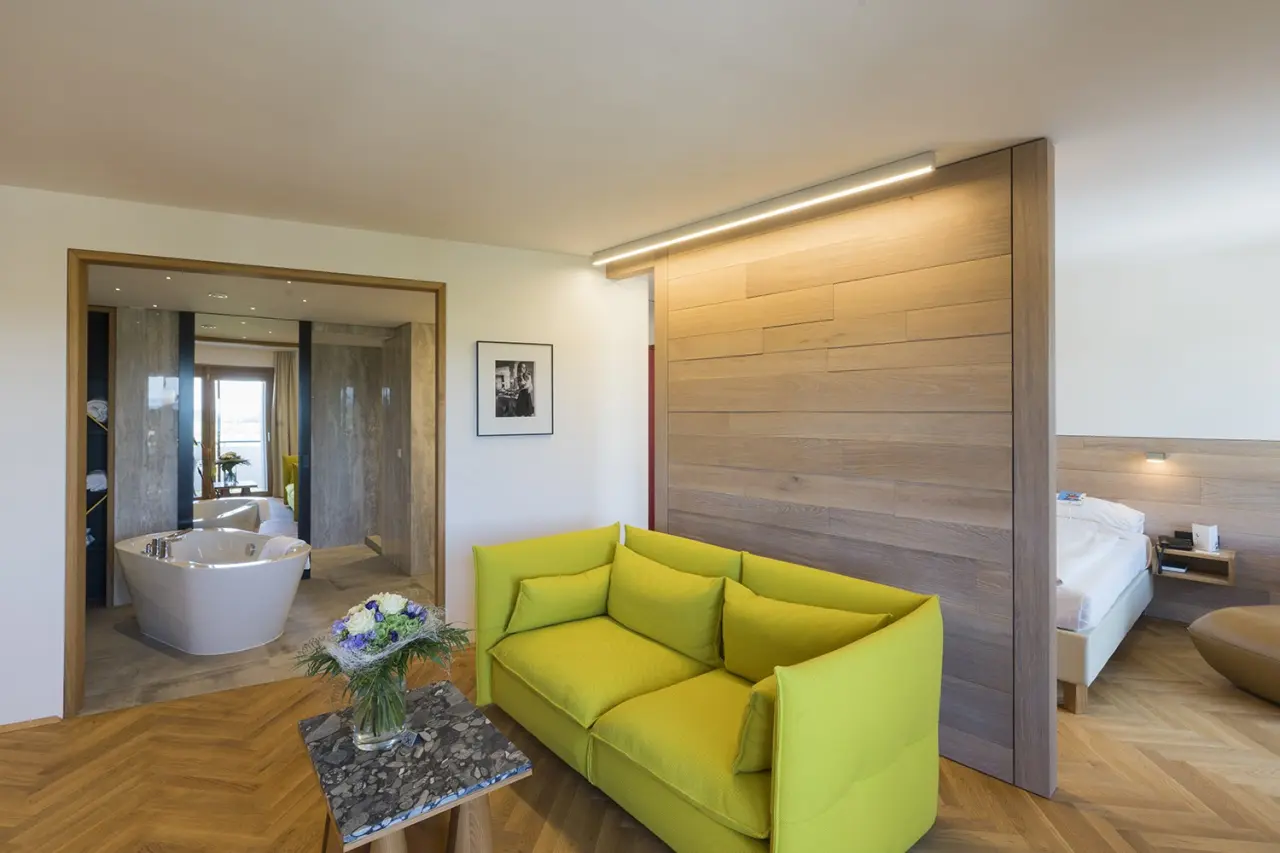 Luxuriöse Suite im Hotel Reiters Finest Family mit stilvollem Wohnbereich, gelbem Sofa und freistehender Badewanne.